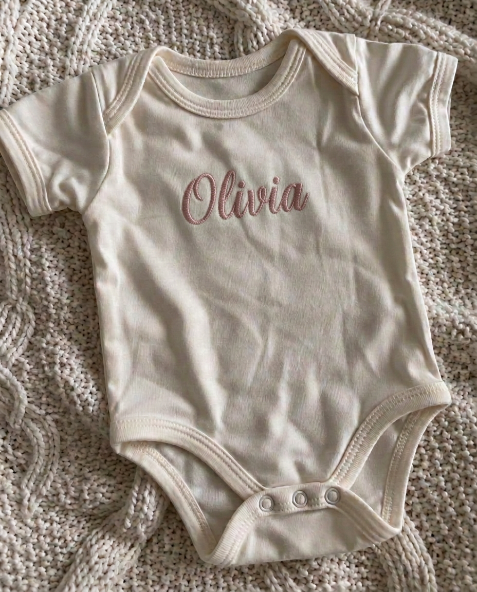 Baby bodysuit with the name Olivia embroidered in dusty-rose script thread