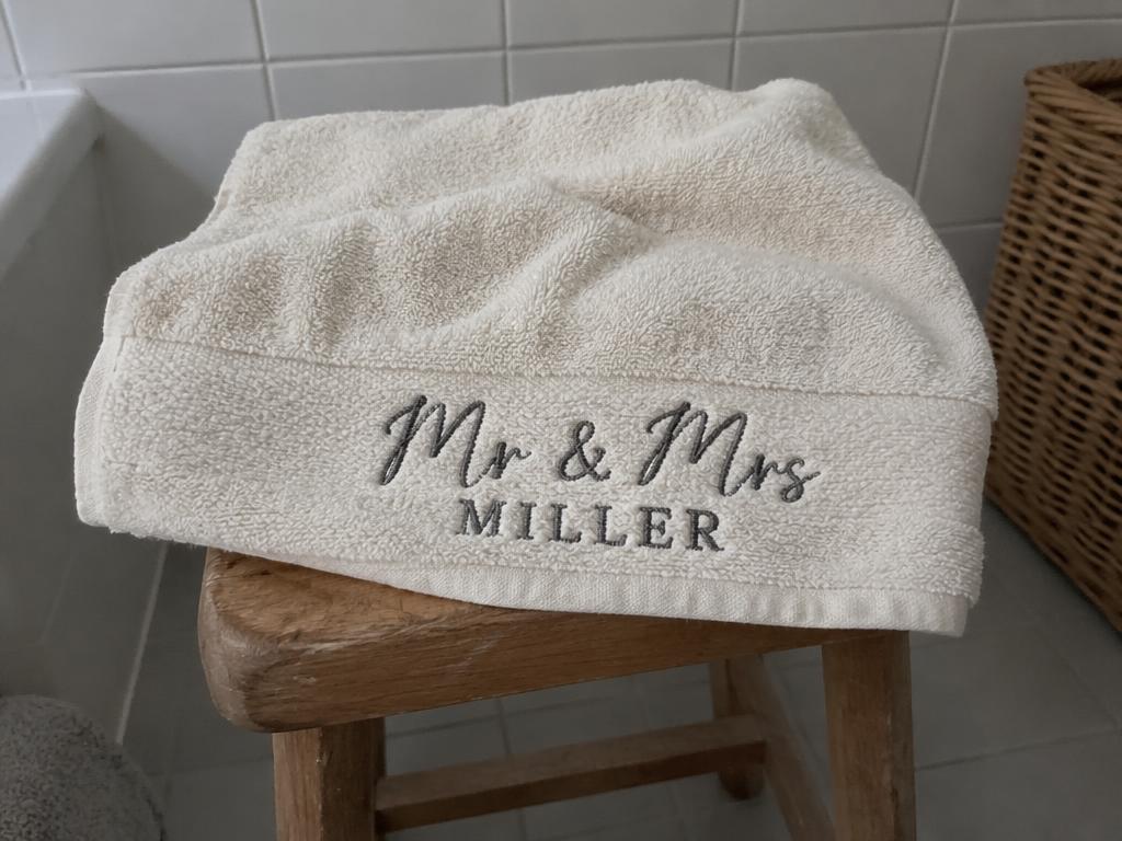 Illustrative photo of a cream bath towel folded on a wooden stool with Mr & Mrs Miller embroidered on the border
